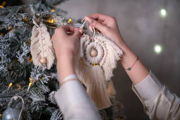 The hands of a girl with a fashionable macrame Christmas ornament decorate a Christmas tree in Scandinavian style. Handmade decoration in boho style. The concept of zero waste. Natural materials - cotton thread. Eco-jewelry, handmade decor las manos de una niña con un adorno navideño de macrame de moda decoran un árbol de navidad en estilo escandinavo. decoración artesanal en estilo boho. el concepto de residuo cero. materiales naturales - hilo de algodón. eco-joyería, decoración hech