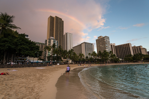 Oahu, USA - Nov 2, 2021: Tourists enjoying the beach as a rainbow form over Waikiki beach late in the day as a storm passes.
