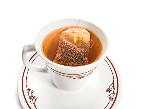 A cup of hot tea on a a chilly day is enjoyable, as freshly brewed tea in a white tea cup with human hand pulling on tea bag on white background with copy space