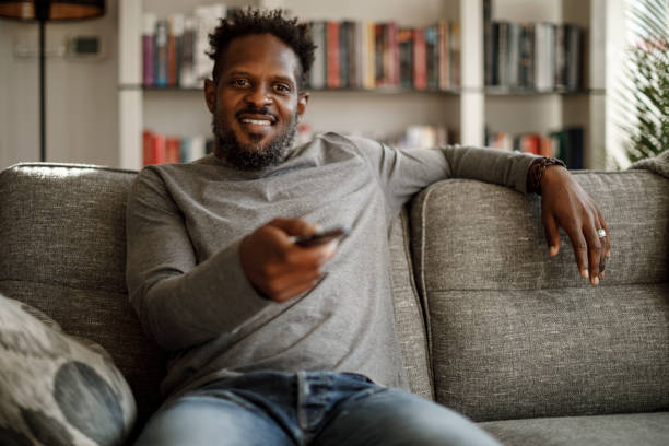 istock Smiling man watching tv using remote controller in living room 1353265969