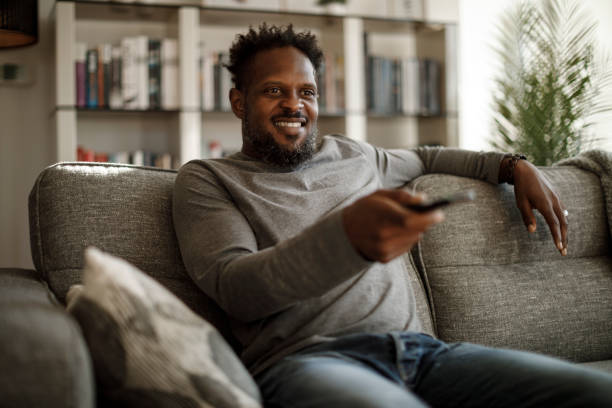 istock Smiling man watching tv using remote controller in living room 1353265970