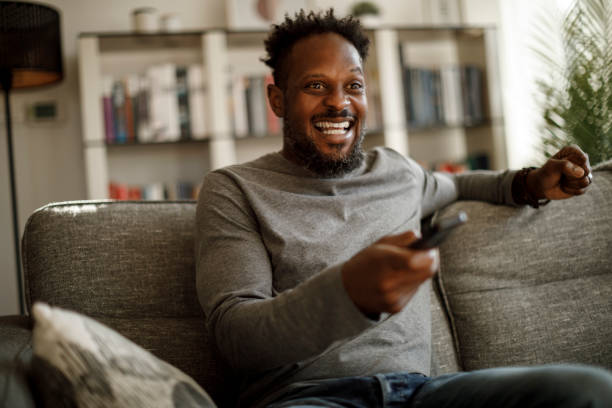 hombre emocionado animando mientras ve la televisión en casa - watching tv fotografías e imágenes de stock