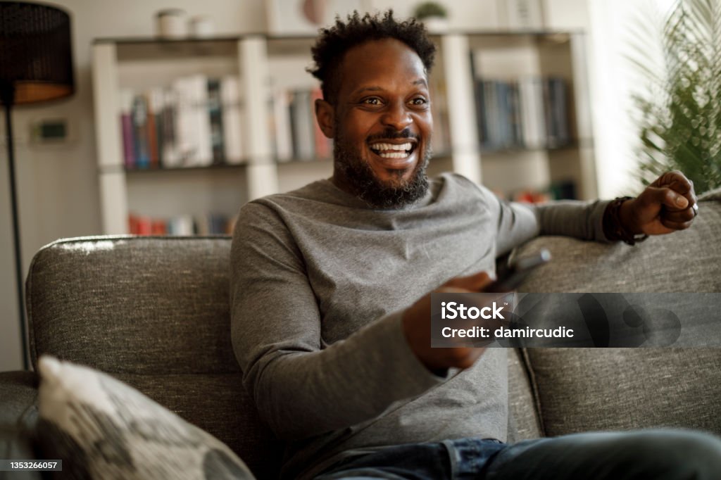 Excited man cheering while watching tv at home Television Set Stock Photo