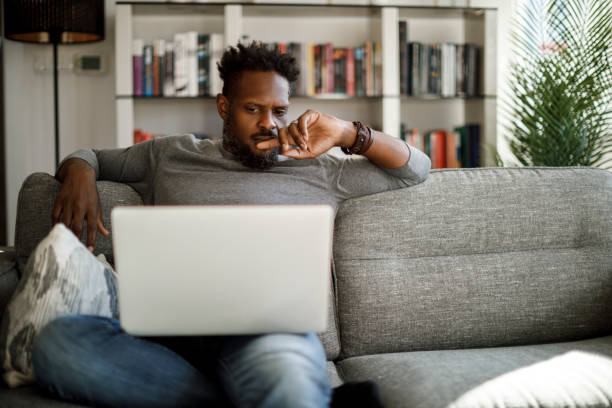 young man watching movie on laptop at home - computer thinking men people imagens e fotografias de stock