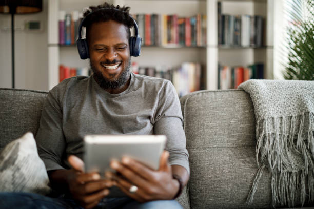 istock Young smiling man with wireless headphones using digital tablet at home 1353266807
