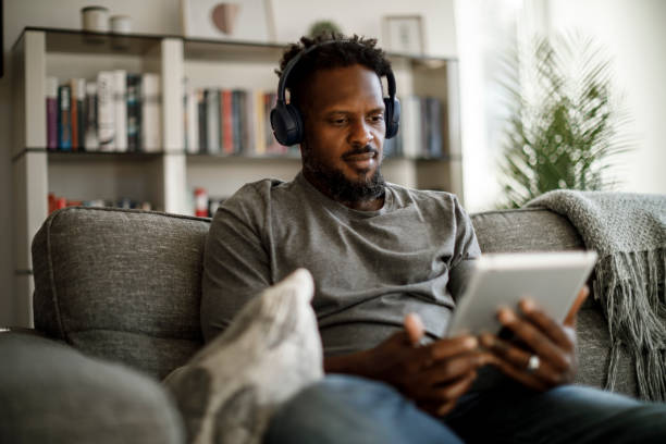 istock Young man with wireless headphones using digital tablet at home 1353266817