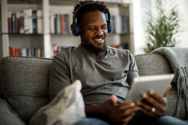 istock Young smiling man with wireless headphones using digital tablet at home 1353266820
