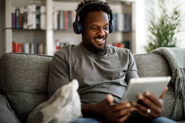 istock Young smiling man with wireless headphones using digital tablet at home 1353266824