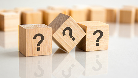 three question marks written on wooden cubes, lying on the gray table, concept