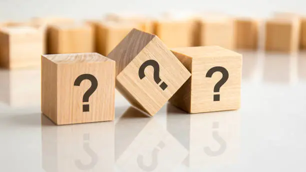 Photo of three question marks written on wooden cubes, lying on the gray table, concept