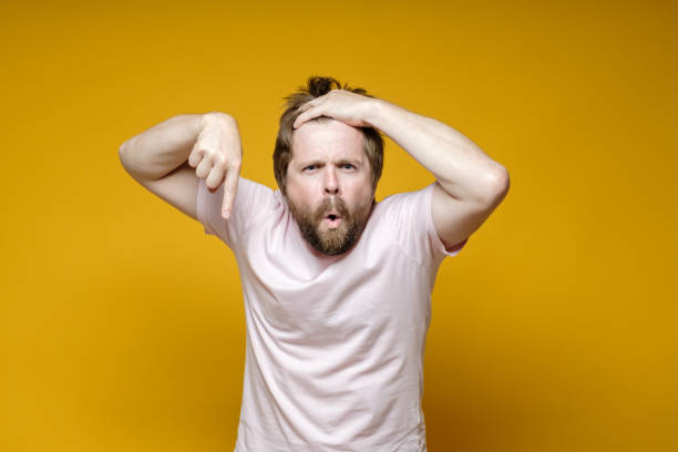 istock Disgruntled, strange man points down with index finger, holds his hair with hands and looks seriously while saying something. 1353268587