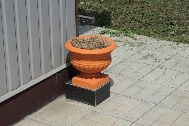 one brown concrete flowerpot with dry vegetation stands on a gray sidewalk in the street against a metal wall