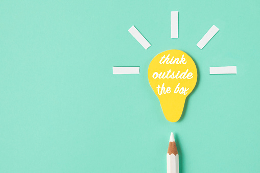Creative composition of white colored pencil with small yellow paper light bulb on green background