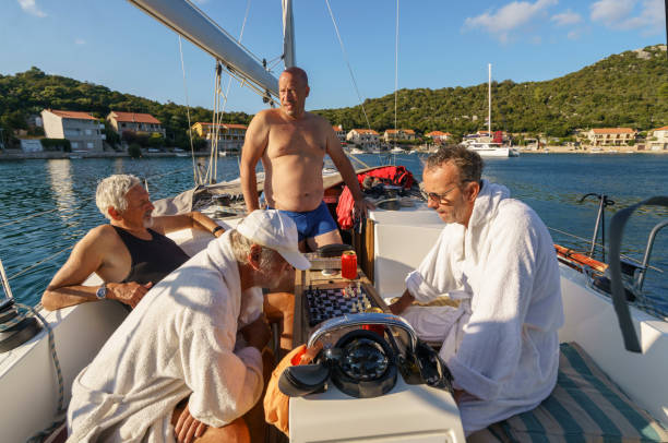 Four men on a sailboat, two enjoying boat life, while two are playing chess