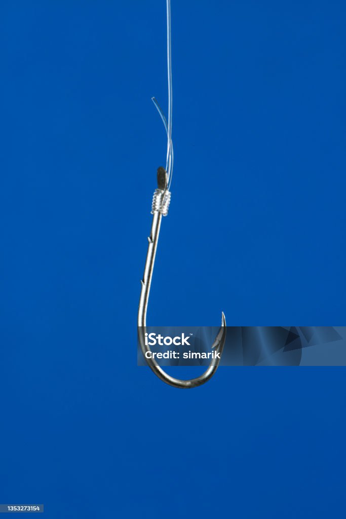 Fishing Hook Fishing hook is hanging with transparent string in front of blue background. Lead Stock Photo