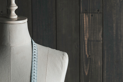 Tailor Mannequin with measure tape in front of wooden wall.