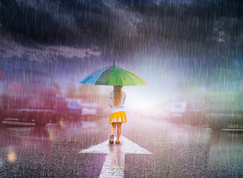 Rear View of a Little Girl Holding an Umbrella and Staying in the Middle of the Street in the Rain Looking at the Dramatic Sky