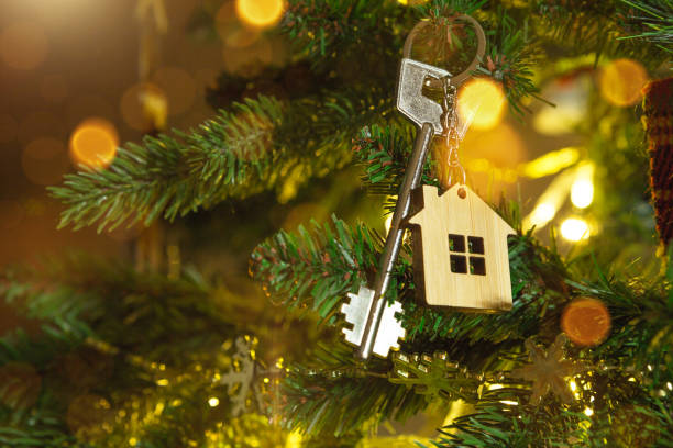 Key to the house with a keychain is hanging on the Christmas tree. A gift for New Year, Christmas. Building, design, project, moving to new house, mortgage, rent and purchase real estate. Copy space stock photo