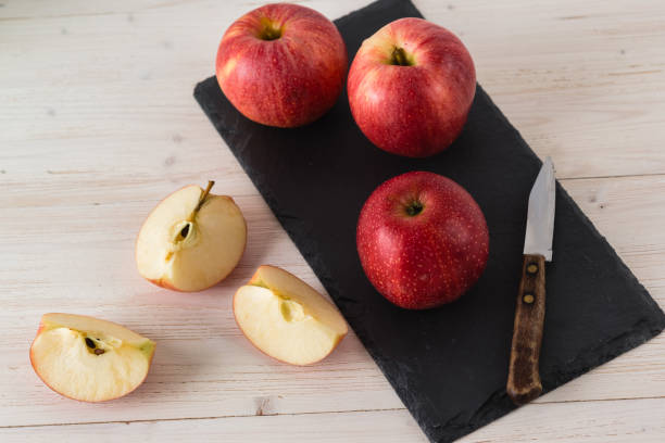 istock In a rectangular black dish on white wooden table are three juicy beautiful ripe red apples of the early winter variety Gala. Next to the slices of the cut fruit and a knife. Top view 1353281310
