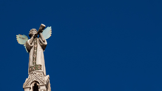 Cherub Angel blowing trumpet. A medieval 13th century statue a the top of St Michael Church in Lucca