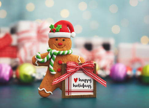 Fondo de Navidad con un hombre de pan de jengibre sosteniendo un letrero de felices fiestas y regalos de Navidad en un entorno verde azulado photo