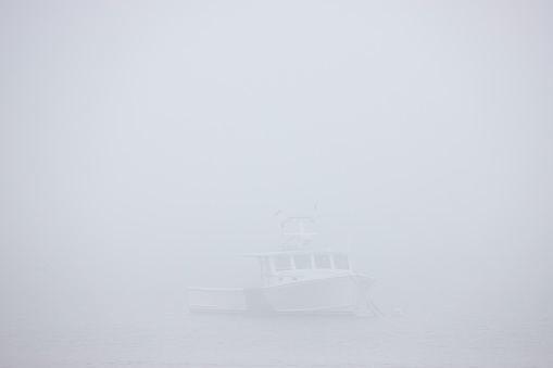Photograph of a boat barely visible through the thick fog.