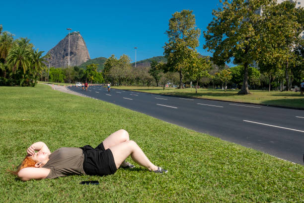 une femme écoute de la musique allongée sur la pelouse du parc - parc flamengo photos et images de collection