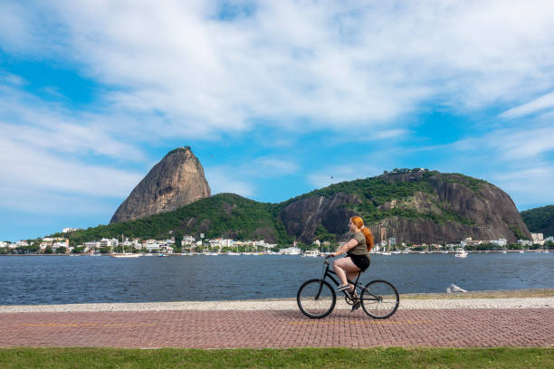 frau fährt fahrrad mit zuckerhut als hintergrund - brazil bicycle rio de janeiro outdoors stock-fotos und bilder
