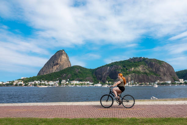 mujer anda en bicicleta con pan de azúcar como fondo - guanabara bay fotografías e imágenes de stock