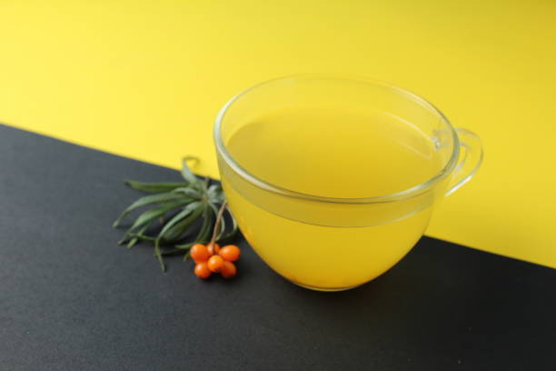sea buckthorn tea drink on a black yellow bright background. Sea buckthorn drink tea juice in a glass cup next to a spout of sea buckthorn leaves orange berries on a black and yellow background. Creative creative photography. Seasonal berry. bebida de té de espino cerval de mar sobre un fondo amarillo negro brillante. el espino cerval de mar bebe jugo de té en una taza de vidrio junto a un pico de espino cerval de mar que deja bayas naranjas sobre un fondo negro y amarillo. fotografía creat