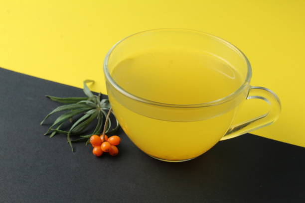 sea buckthorn tea drink on a black yellow bright background. Sea buckthorn drink tea juice in a glass cup next to a spout of sea buckthorn leaves orange berries on a black and yellow background. Creative creative photography. Seasonal berry. bebida de té de espino cerval de mar sobre un fondo amarillo negro brillante. el espino cerval de mar bebe jugo de té en una taza de vidrio junto a un pico de espino cerval de mar que deja bayas naranjas sobre un fondo negro y amarillo. fotografía creat