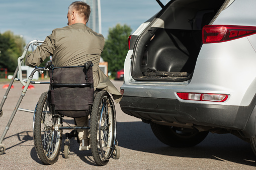 Back view of adult man using wheelchair unloading car in parking lot outdoors, copy space