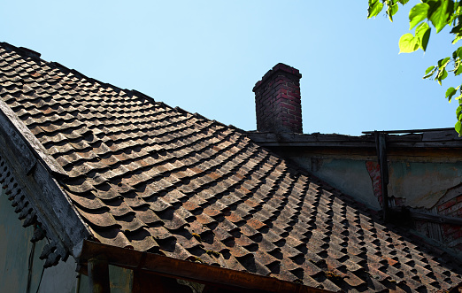View of tiled roof at old german house with brick tube, blue sky and green leaves