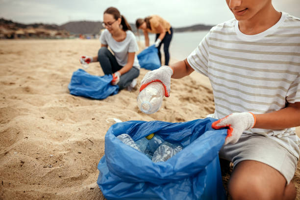des bénévoles nettoient la plage en ramassant les ordures dans un sac en plastique - water child bottle little boys photos et images de collection