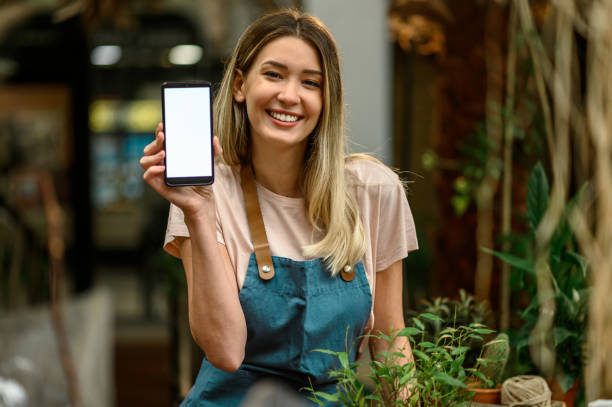 mujer florista trabajando en una tienda de flores y mostrando la pantalla de un teléfono inteligente - florist telephone flower business fotografías e imágenes de stock