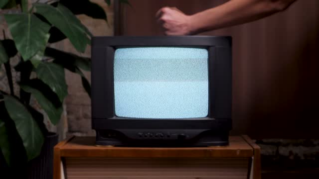 Man hitting old TV screen close up. 80s home interior old television set. Bad television signal noise. No signal tv turning on screen hand knocking retro static noise. Analog static effect retro tv