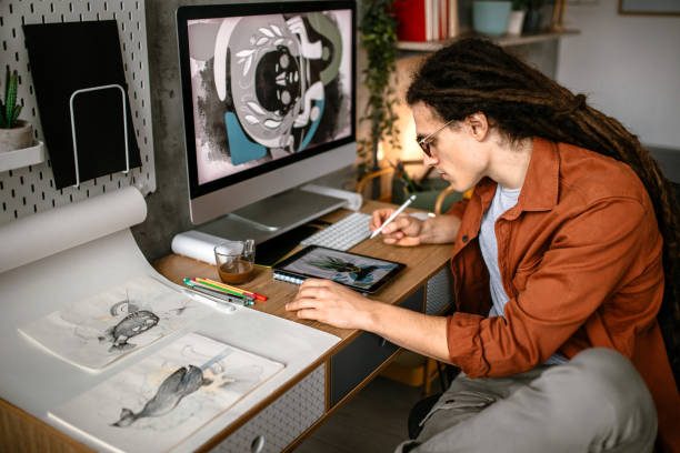 Creative graphic designer using digital tablet and computer Young graphic designer with long hair working in his studio. Sketching using drawing pad person drawing on tablet stock pictures, royalty-free photos & images