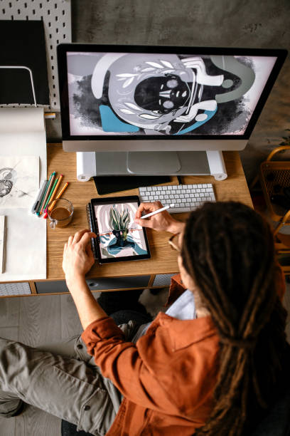 Creative graphic designer using digital tablet and computer, creating new design solutions Young graphic designer with long hair working in his studio. Sketching using drawing pad person drawing on tablet stock pictures, royalty-free photos & images