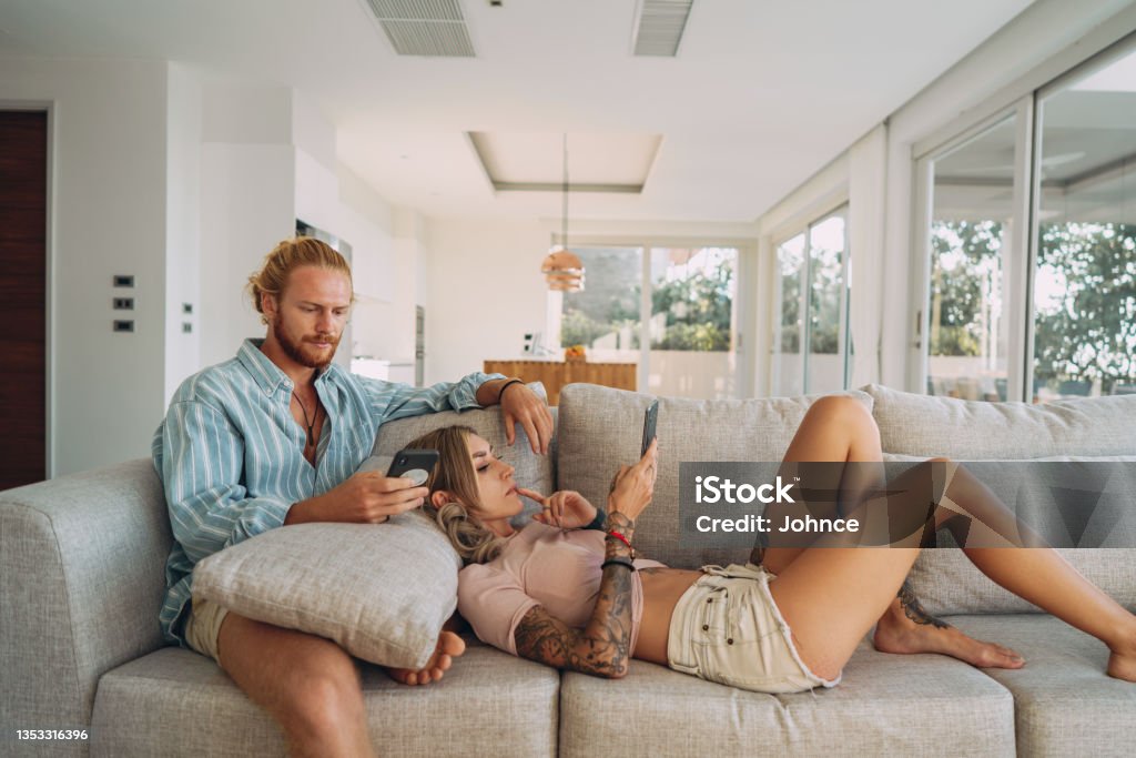 Couple using phones at home Couple is on the couch in living room, using their phones. Boredom Stock Photo