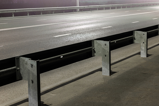 illuminated empty foggy night road with rigid guardrails, traffic barriers or crash barriers
