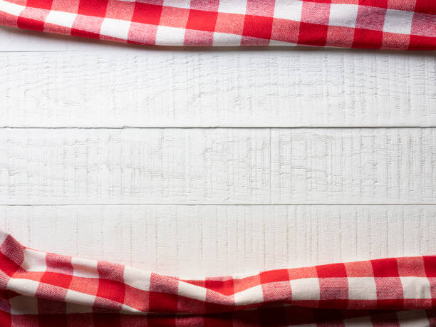 istock White textured wood table with quality natural cotton red square gingham pattern tablecloths at the top and the bottom of the image. 1353318261