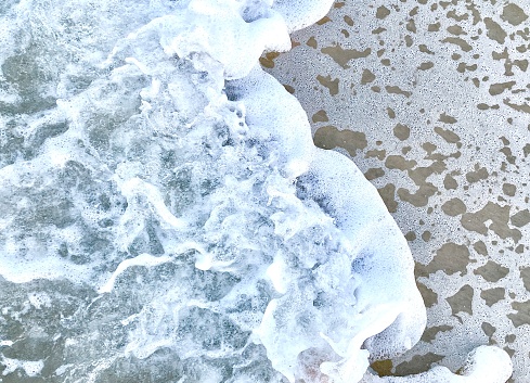 Horizontal close up of patterned design in nature's white sea salt water foam of shoreline wave on high tide sand of beach walk