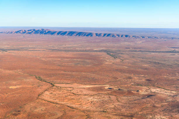 This elevated view captures the striking contrast between the rich red earth and the scattered greenery of arid vegetation, with pale yellow grasses stretching into the distance.
