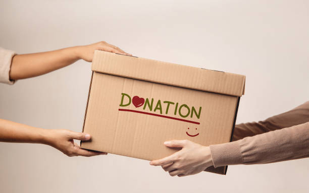 Donation Concept. The Volunteer Giving a Donate Box to the Recipient. Standing against the Wall stock photo