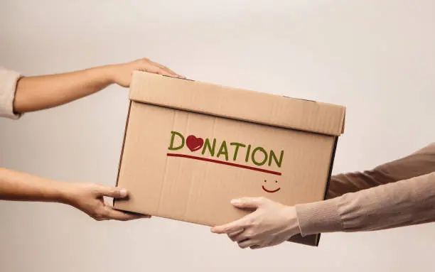 Photo of Donation Concept. The Volunteer Giving a Donate Box to the Recipient. Standing against the Wall