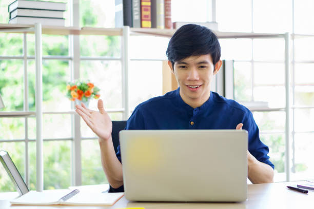 Smiling asian man looking at camera on laptop computer, recording self-presentation video or sharing professional skills. Happy young smart people filming educational lecture.
