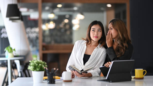 Young business woman whispering in ear of her colleague. Young business woman whispering in ear of her colleague. whispering stock pictures, royalty-free photos & images