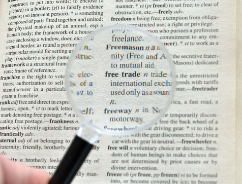 Closeup of a magnifying glass hovering over free trade in a mass produced dictionary.