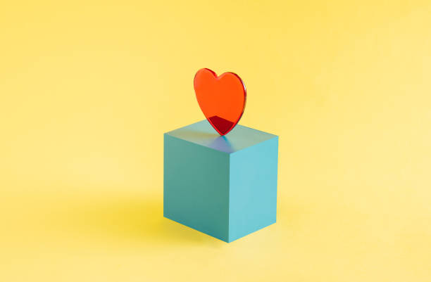 istock A red heart set on a blue cube isolated on a yellow background. Valentine's Day 1353337536