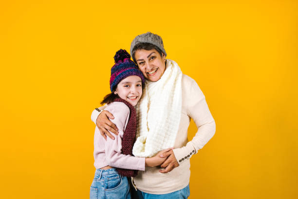 winter portrait of happy latin family grandmother and granddaughter on yellow background in mexico latin america - senior adult winter senior women daughter imagens e fotografias de stock